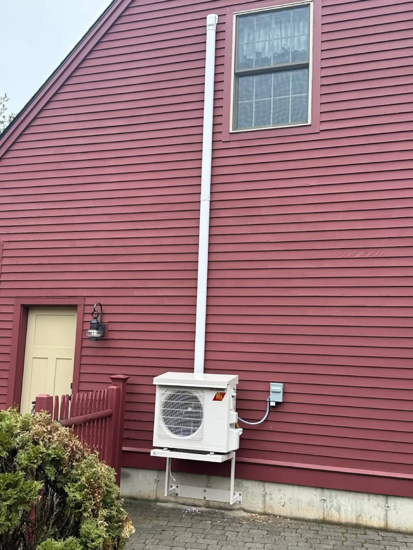 Wide view of an outdoor heat pump unit and refrigerant line set on a home exterior