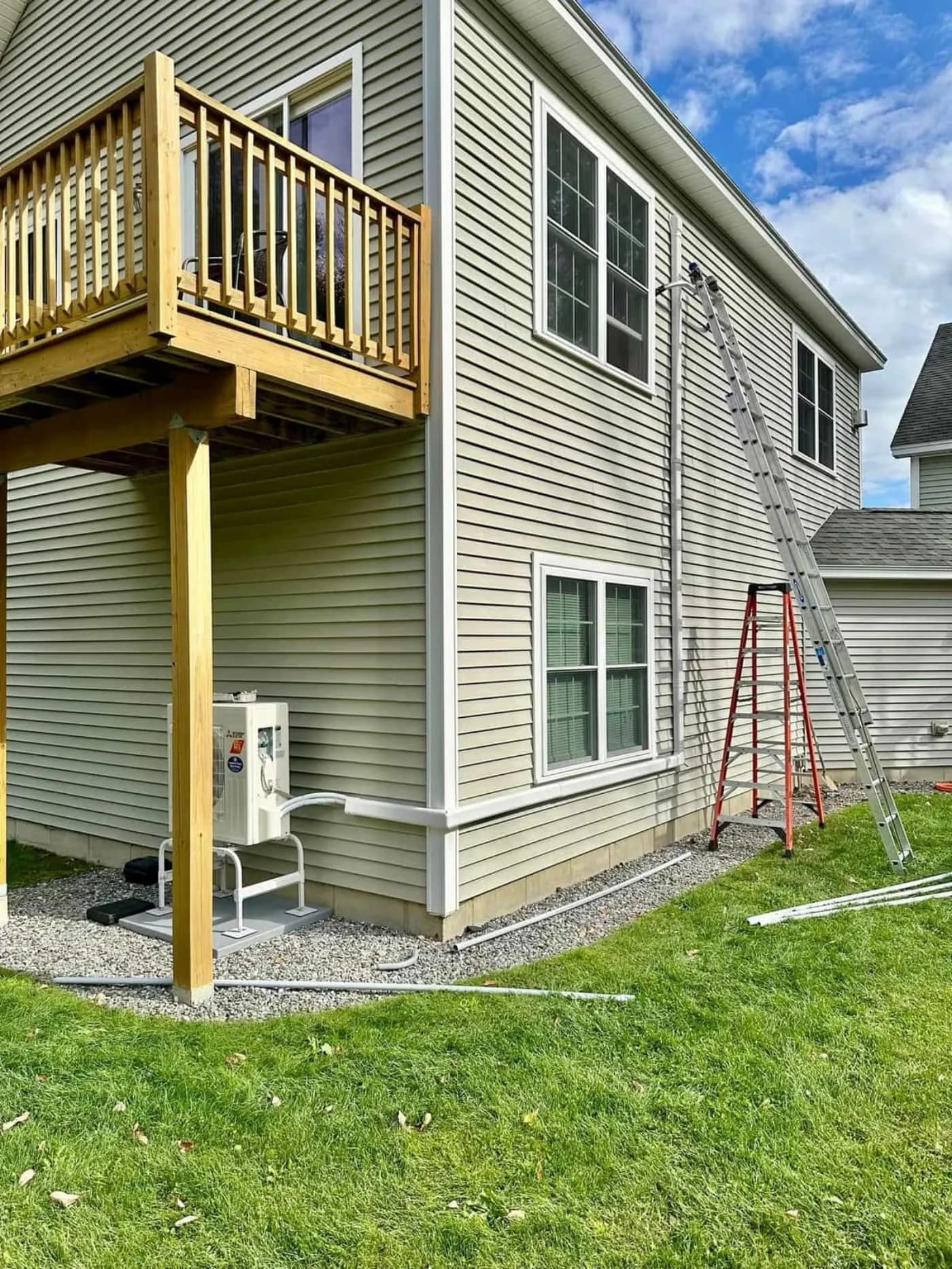 Mitsubishi ductless outdoor unit installed beneath a raised deck on a two-story Southern Maine home