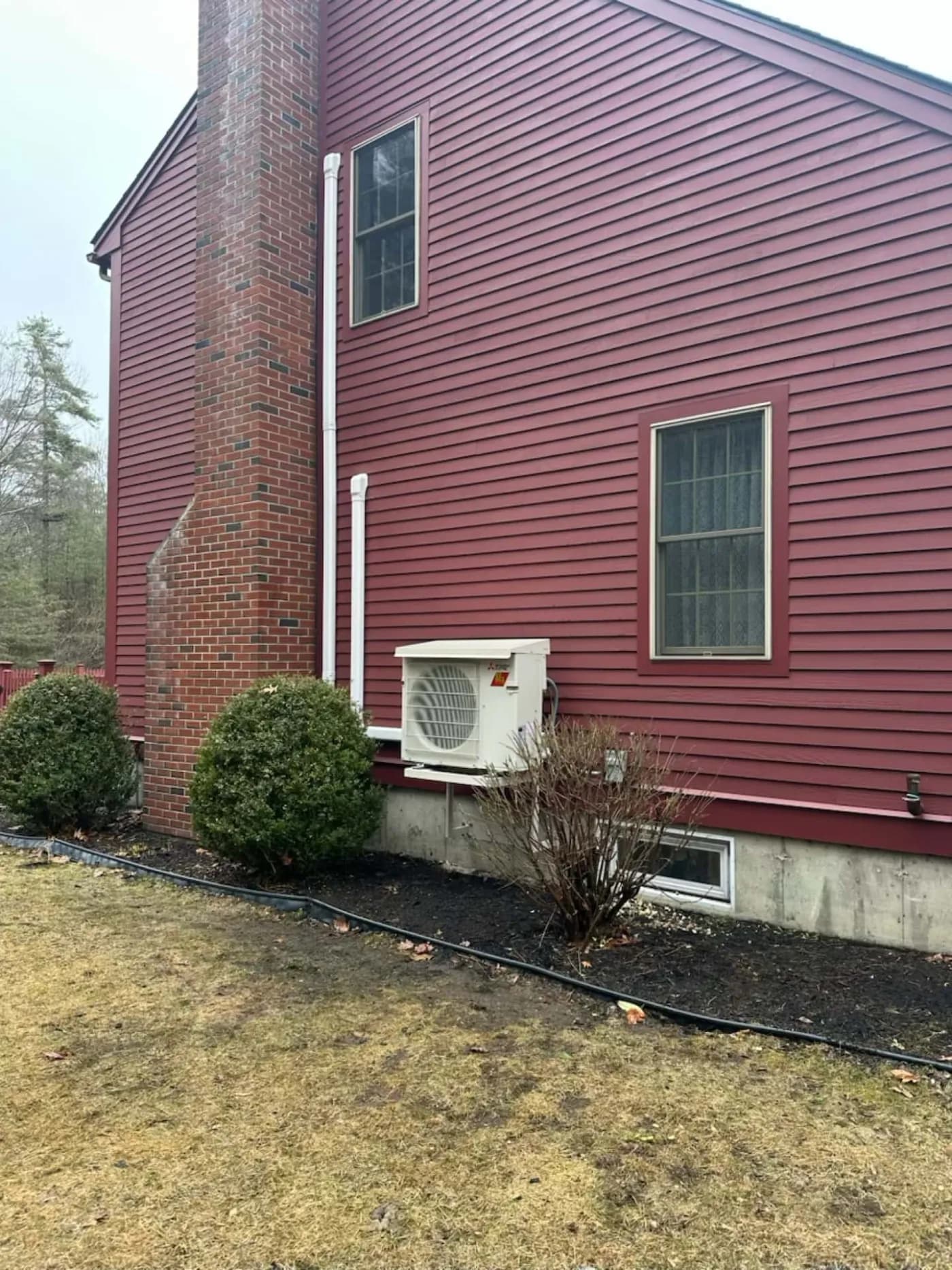 Outdoor heat pump unit mounted on a red residential home with clean line-set routing