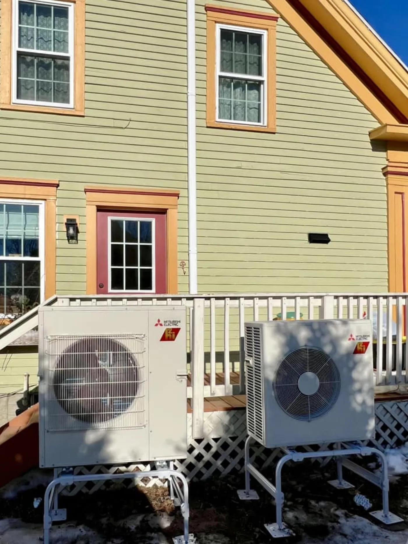 Two Mitsubishi outdoor mini-split condensers installed on stands beside a Maine home