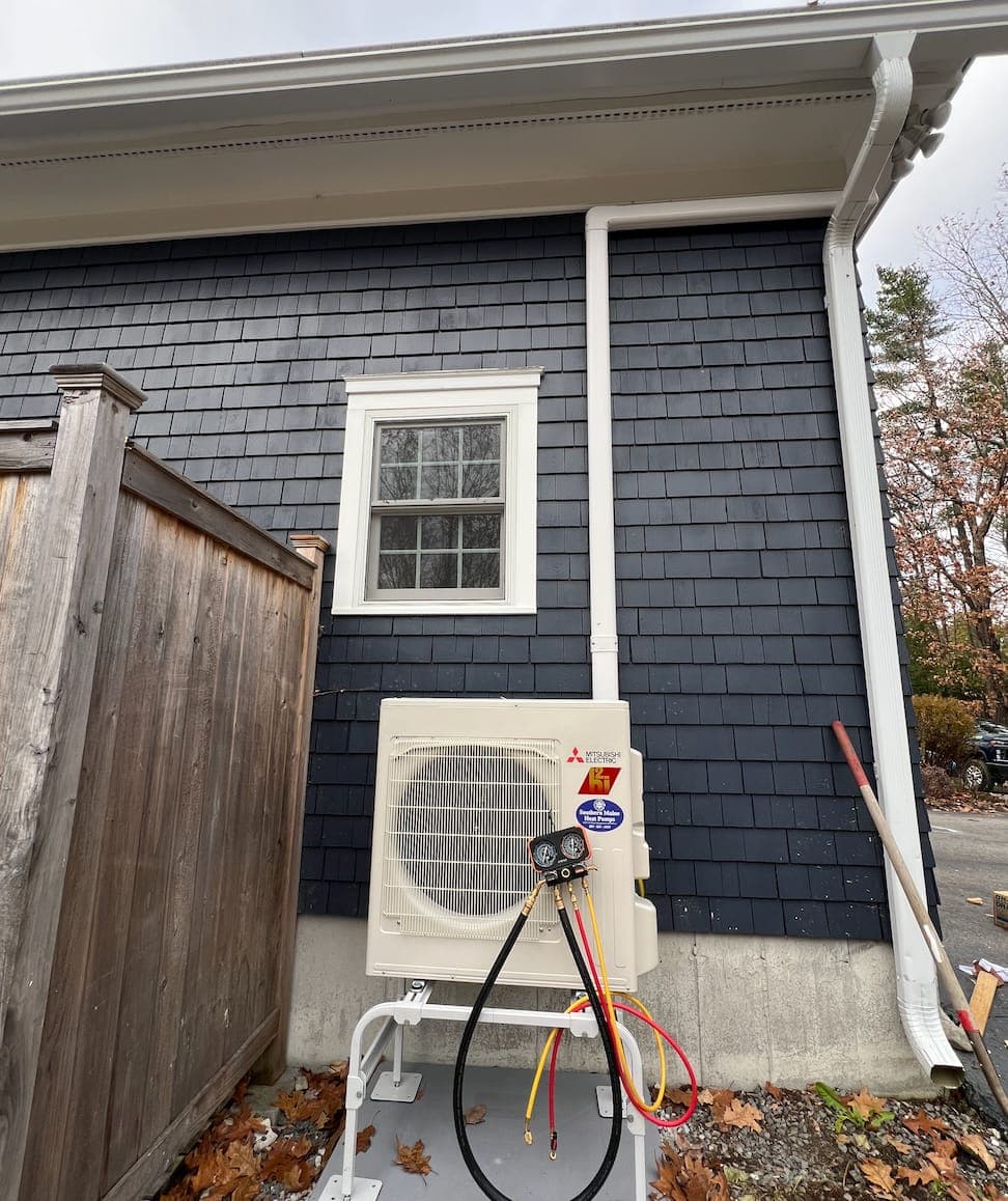 Heat pump technician diagnosing an outdoor unit in Portland, Maine