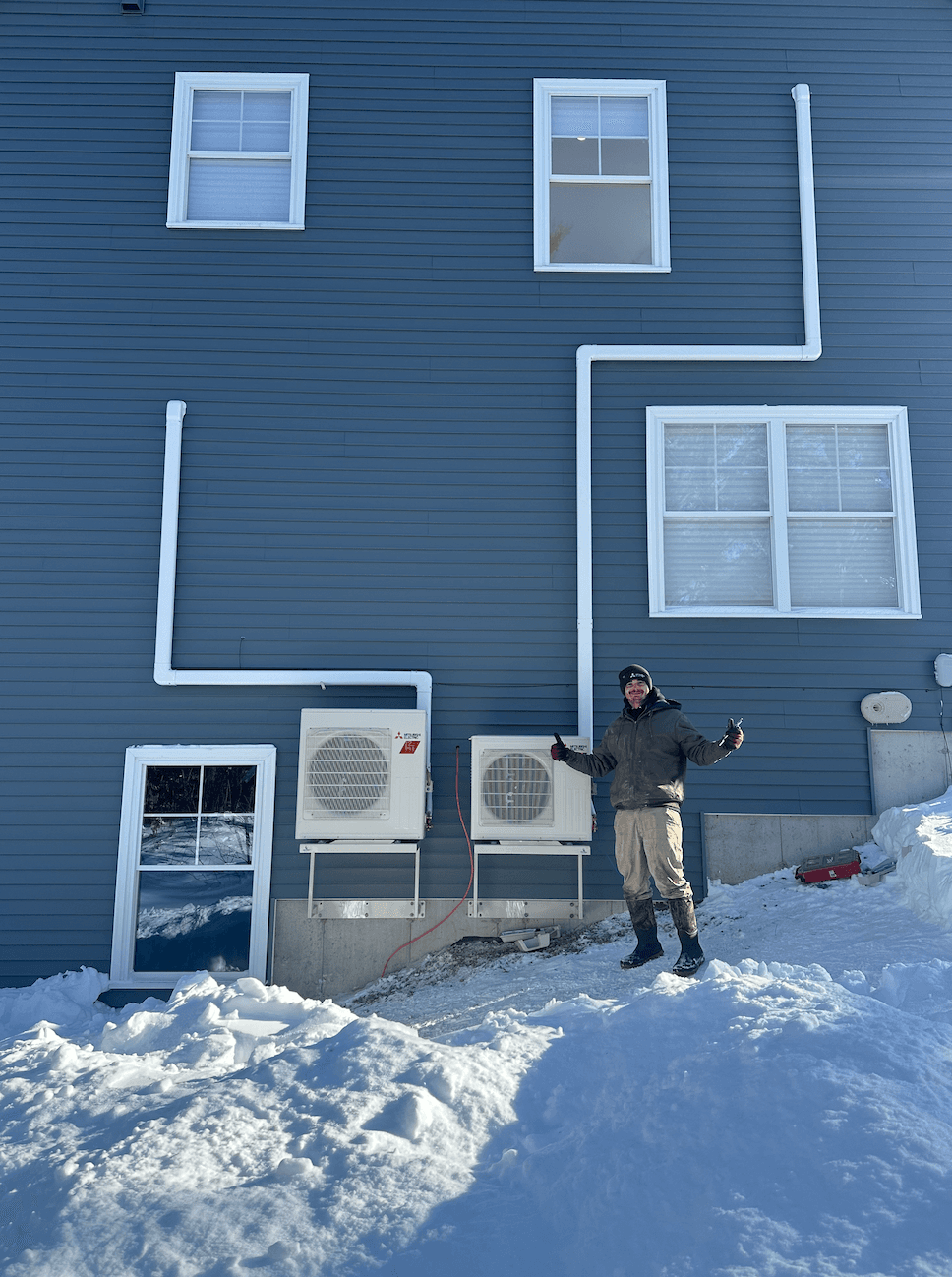 Southern Maine Heat Pumps technician with dual Mitsubishi outdoor units installed in winter