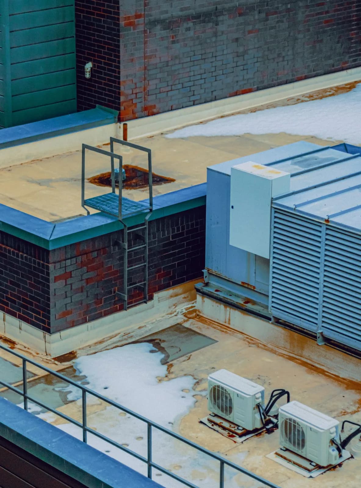 Two outdoor condenser units on a commercial rooftop beside a brick parapet