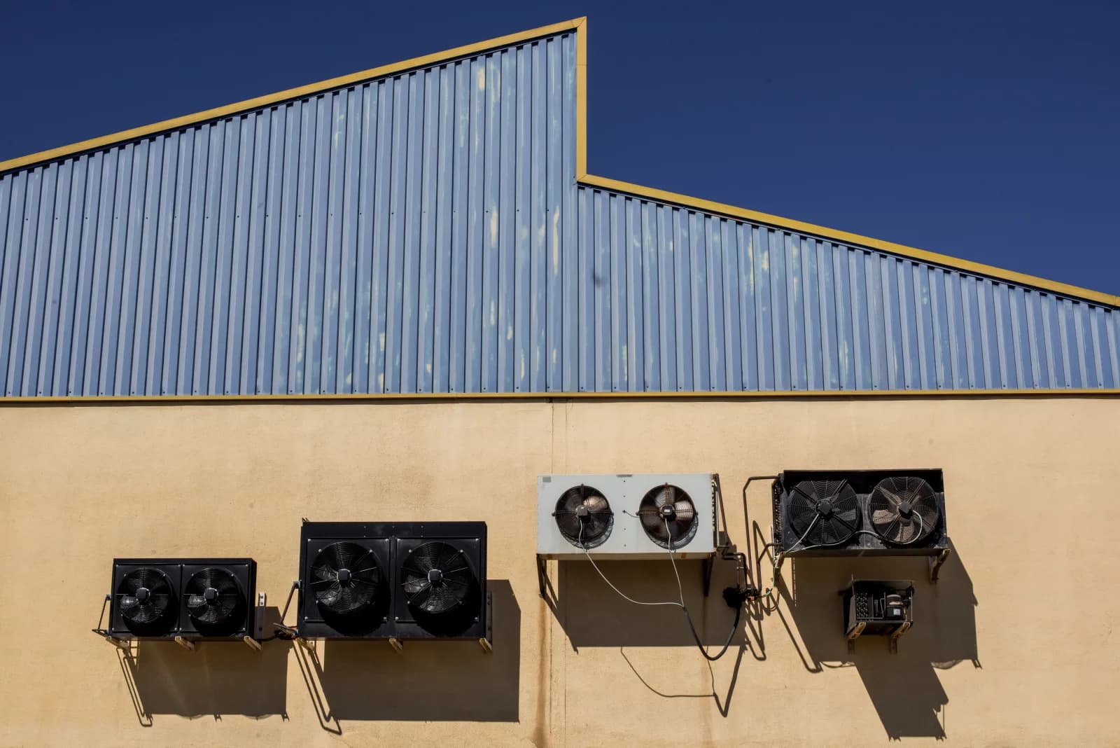 Row of outdoor condenser units mounted beside a commercial building wall