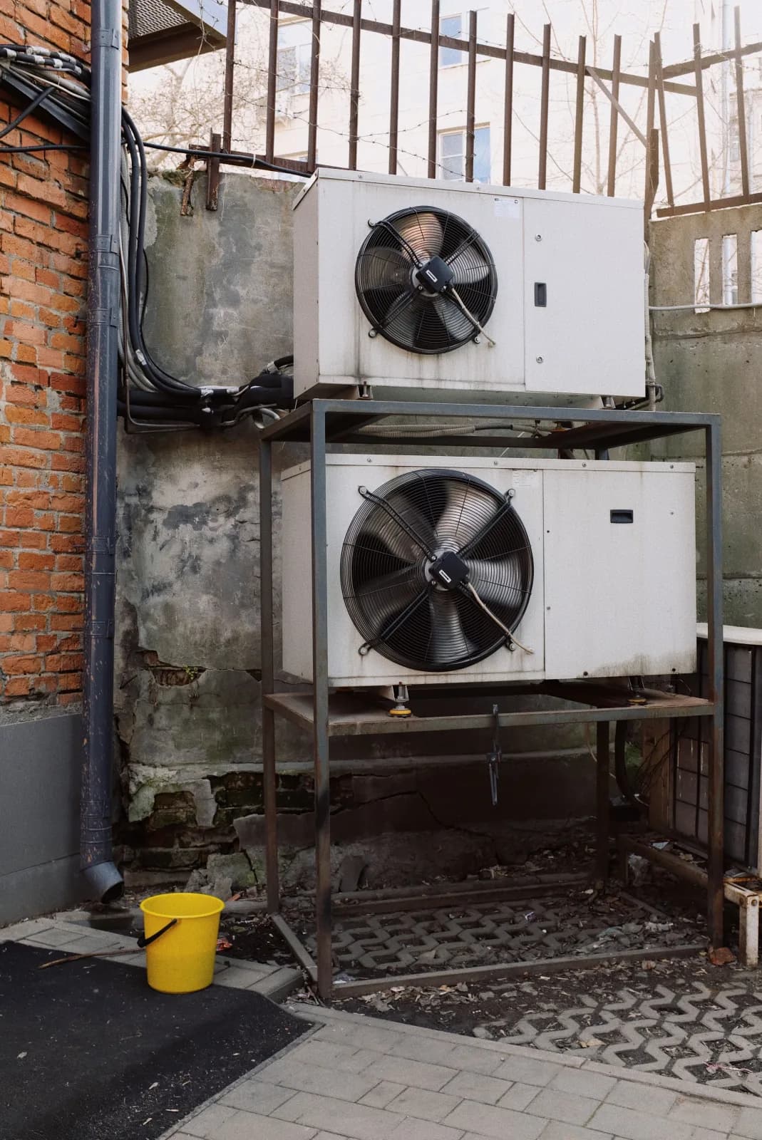 Two industrial condenser units racked against a brick commercial building wall