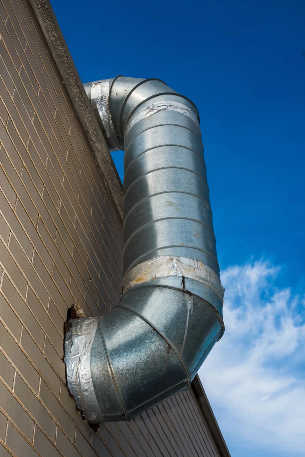 Insulated round duct elbow penetrating a brick exterior wall