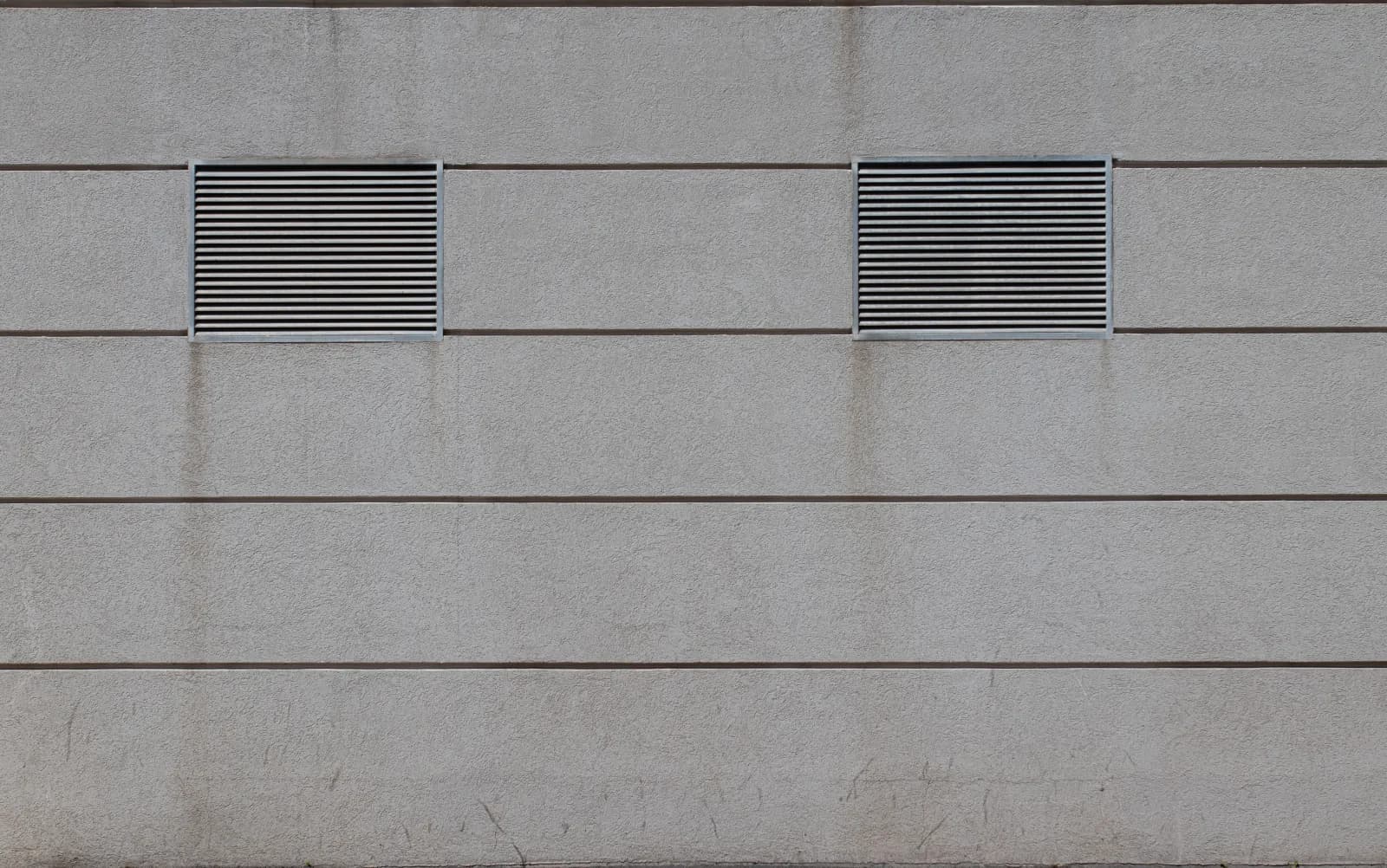 Two louvered exhaust vents set into a concrete commercial building wall