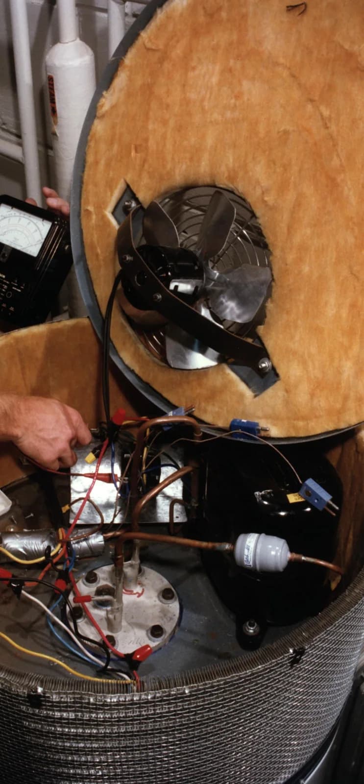 Heat pump water heater's top module opened, showing the fan and motor that pull heat from room air