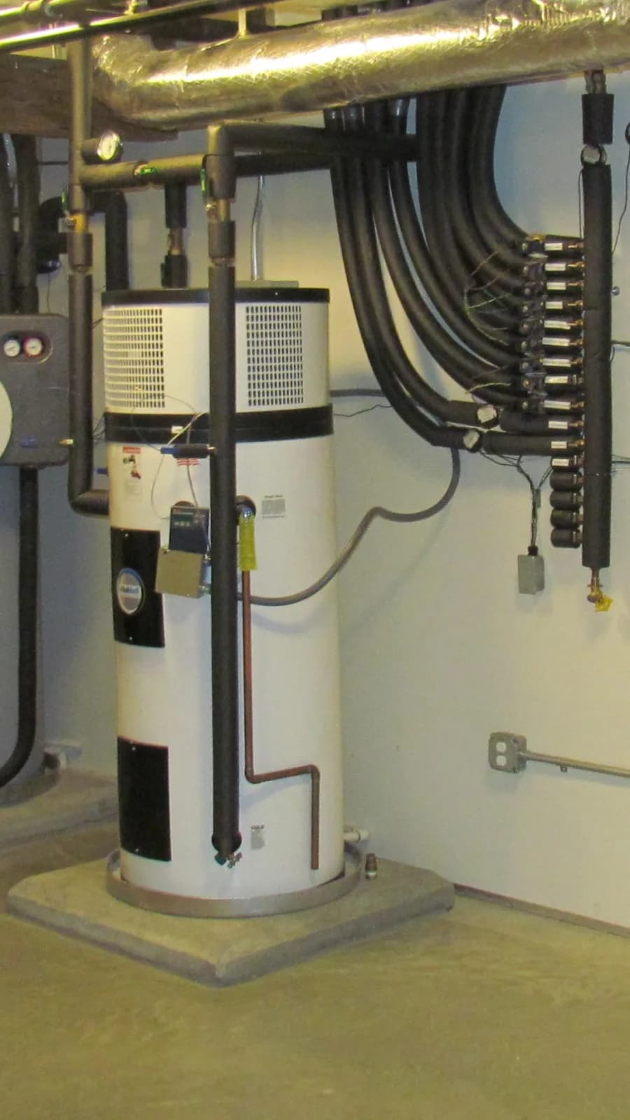 Close-up of a heat pump water heater's fan-topped module and mechanical room piping